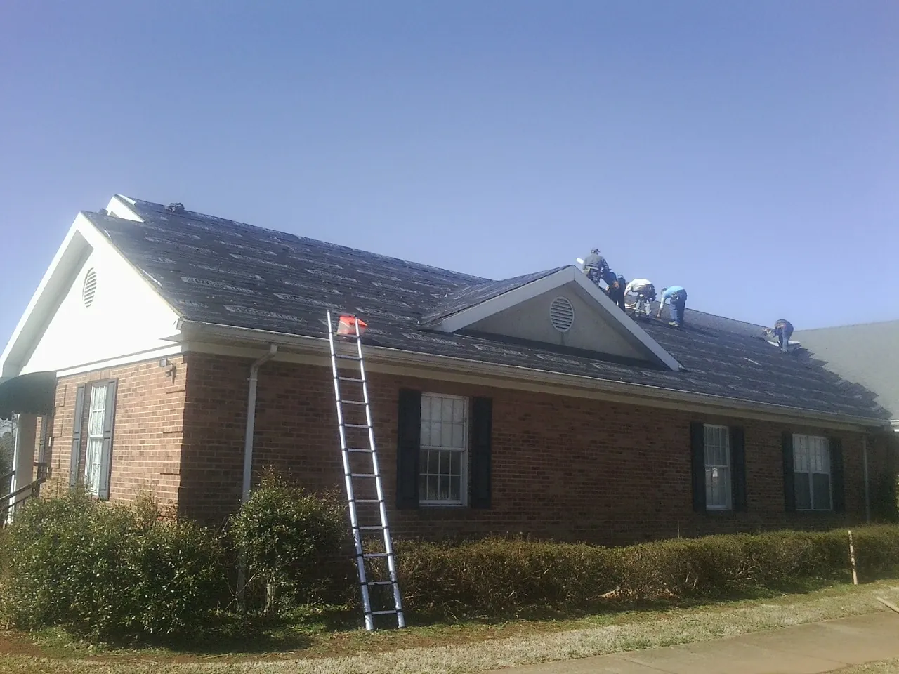 Crew tearing shingles off a brick ranch roof with a ladder set — Metal Roof Repair work by our crew in Caldwell
