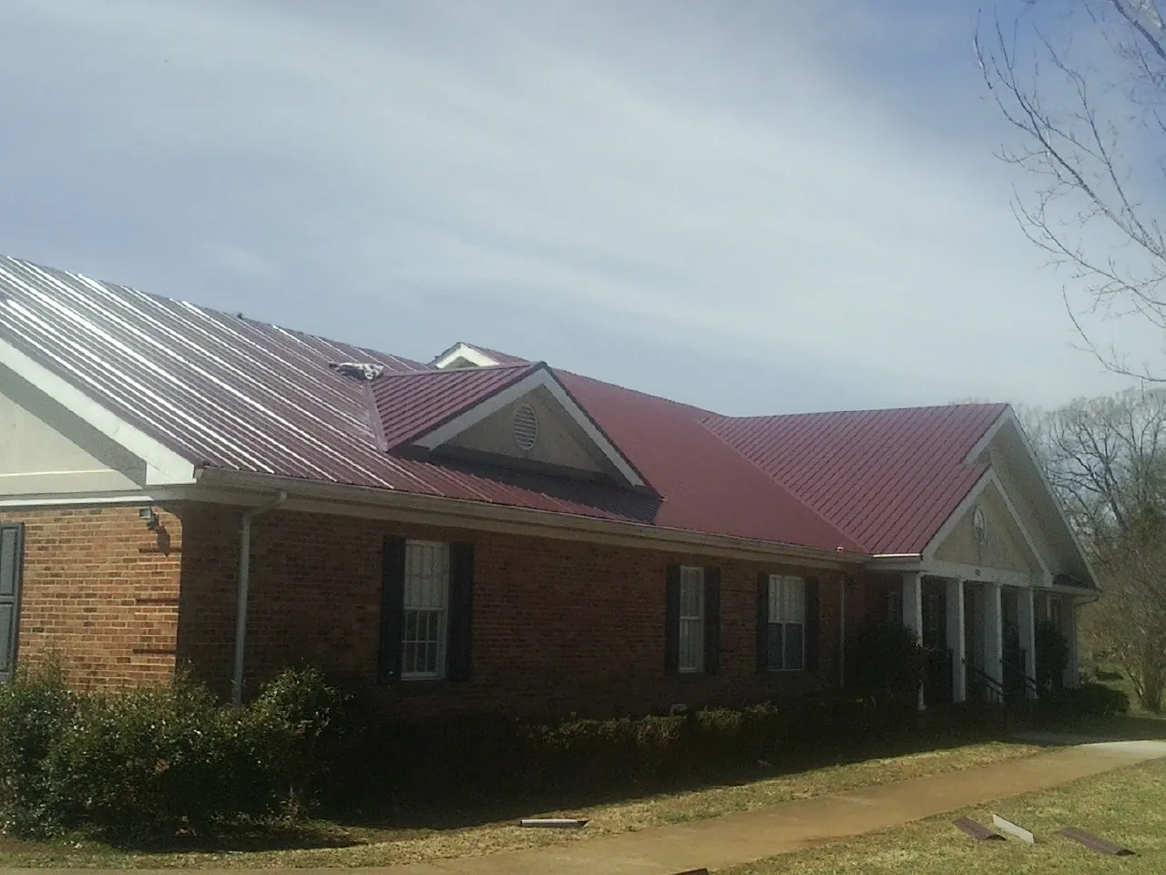 Red metal roof with gabled entries on a long brick building, from a Hail Damage Roof Repair job in Caldwell